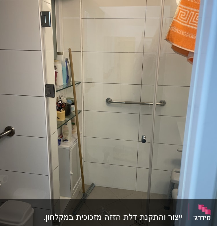 מקלחון עם דלת זכוכית, מגב ומדף עם מוצרים